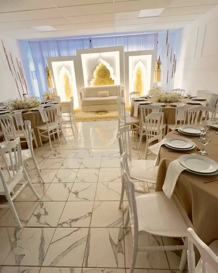 La salle Amoria dressée pour une réception : tables rondes en nappes champagne, chaises Napoléon blanches et arches orientales lumineuses